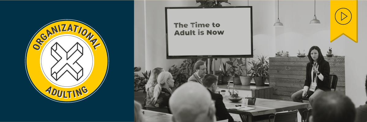 Header image of a black and white photo showing a person holding up two fingers, seated in front of a group at a table next to a screen that reads “The Time to Adult is Now”. A circular yellow badge sits to the left reading “Organizational Adulting” with an inner white circle with the XPLANE logo. Above is a yellow tag with a black play button icon denoting that this webinar has a recording available.