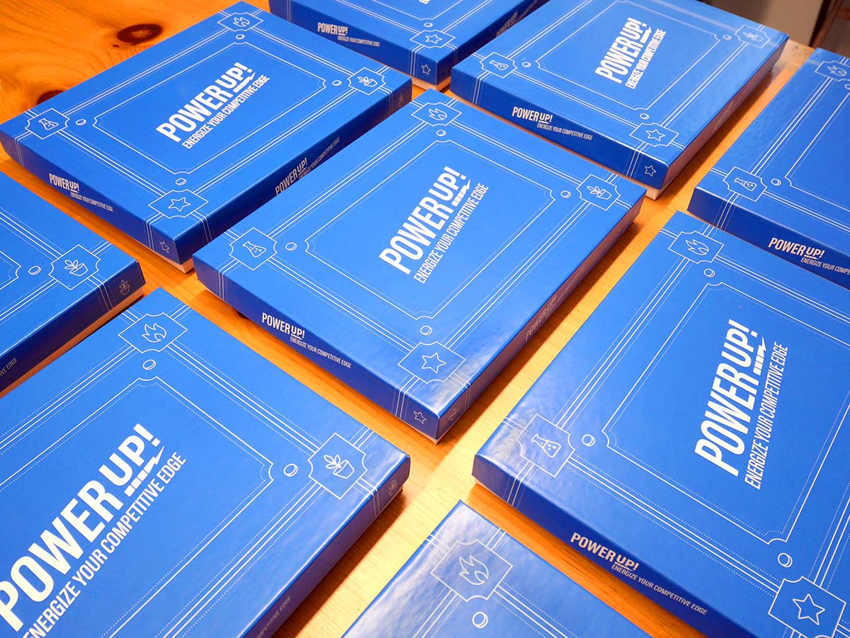 Nine blue game board boxes reading "Power Up!" sit on a wooden table.